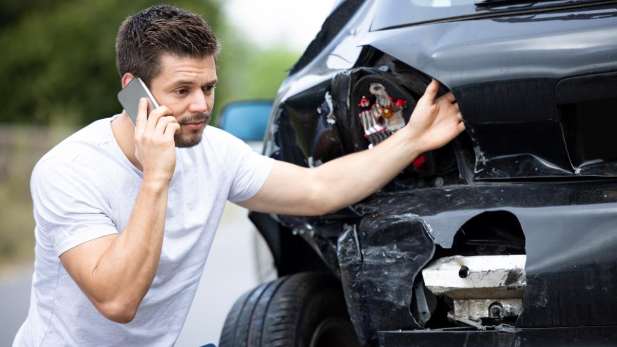 Homem ao telefone avaliando danos em carro batido, ilustrando o processo de como acionar o seguro do carro passo a passo.