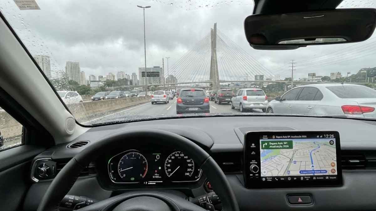 Visão do motorista dentro de um Honda HR-V 2024 em São Paulo, com chuva no para-brisa e trânsito na Marginal Pinheiros, destacando a tela multimídia com informações sobre o seguro auto em São Paulo.