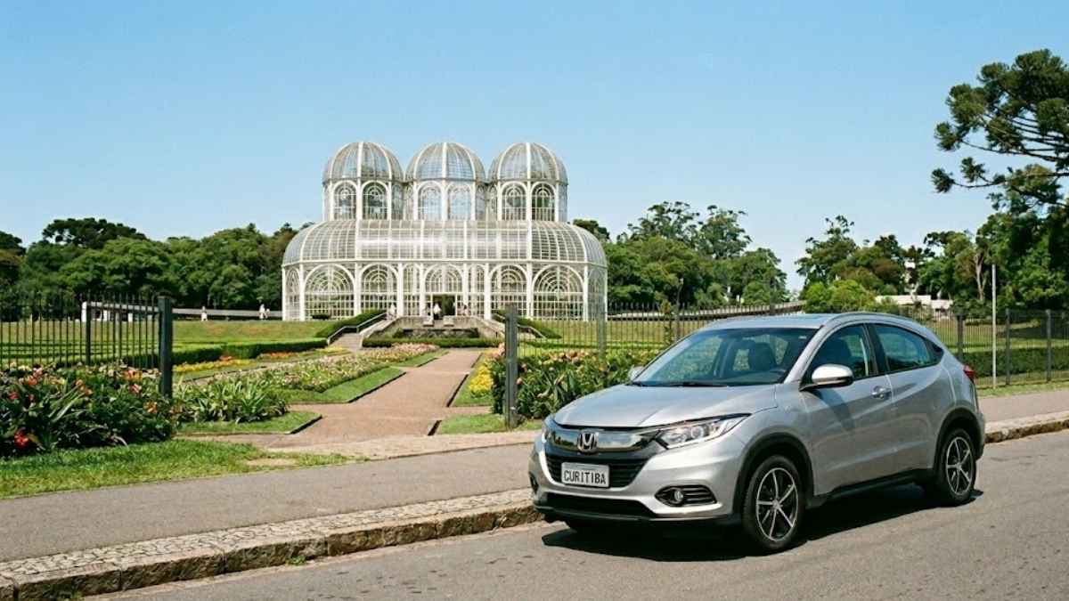 Um SUV prateado estacionado em frente ao Jardim Botânico de Curitiba, com a icônica estufa de vidro ao fundo, uma árvore Araucária e o letreiro "CURITIBA" na placa do veículo. A imagem evoca a proteção e a tranquilidade de quem contrata um seguro auto em Curitiba.
